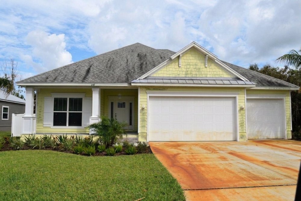 Palm Coast home with algae streaking across the roof, dirty siding and heavy rust staining on the driveway